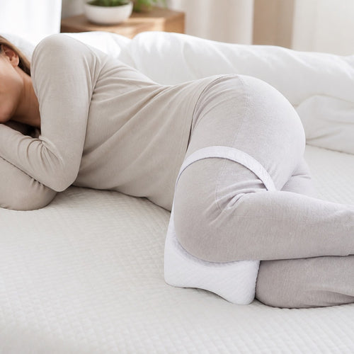 Woman sleeping on her side with the white AlignaFit knee pillow strapped between her knees